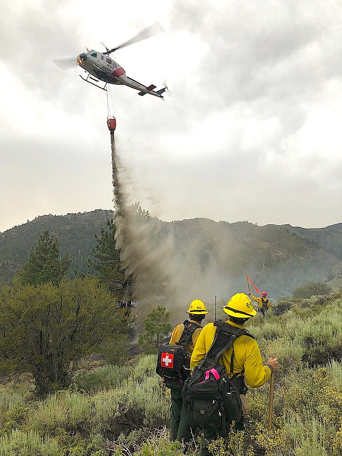 A helicopter dropping a bucket of water on the Swauger Fire as two firefighters look on. U.S. Forest Service photo