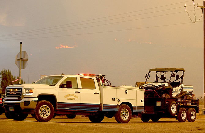 Storey County firefighters pull out of camp to fight the Tamarack Fire as flames are visible in the background