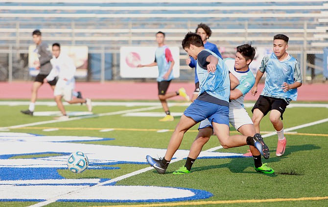 Juniors Michael Catalan, middle, and Miguel Vargas, far right, battle for possession during a Carson High boy’s soccer practice Wednesday.