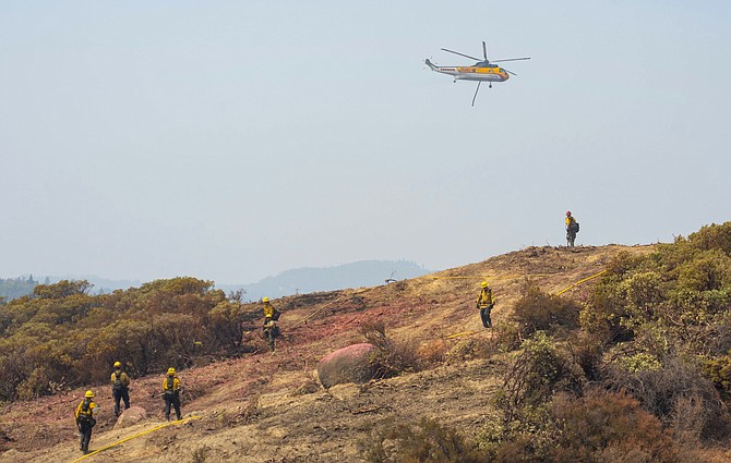 A Croman Sikorsky S-61A helicopter flies over firefighters working on a containment line on the south end of the Caldor Fire west of Grizzly Flats, Calif., on Monday. (Sara Nevis/The Sacramento Bee via AP)
