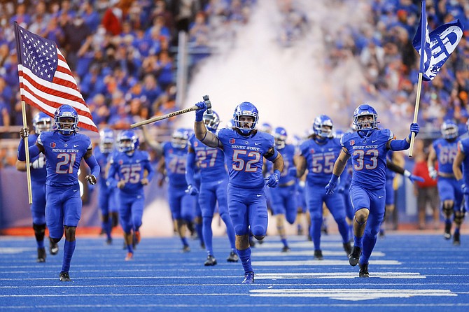 Boise State linebacker DJ Schramm (52), carrying the Dan Paul Hammer, running back Tyler Crowe (33), right, carrying the Bleed Blue flag, and Boise State safety Tyreque Jones (21), left, carrying the American flag, lead Boise State on to the field to face Oklahoma State on Sept. 18, 2021, in Boise, Idaho. Oklahoma State won 21-20. (AP Photo/Steve Conner)