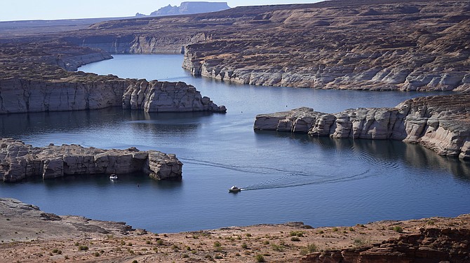 FILE - In this Saturday, July 31, 2021 file photo, a boat cruises along Lake Powell near Page, Ariz. This summer, the water levels hit a historic low amid a climate change-fueled megadrought engulfing the U.S. West.  Severe drought across the West drained reservoirs this year, slashing hydropower production and further stressing the region’s power grids. And as extreme weather becomes more common with climate change, grid operators are adapting to swings in hydropower generation.(AP Photo/Rick Bowmer)