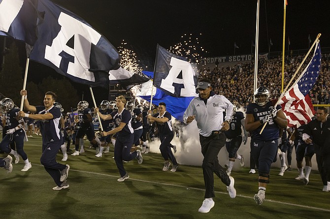 Jay Norvell (at right, white pullover) leads the Wolf Pack into Mackay Stadium to face UNLV on Oct. 29, 2021. (AP Photo/Tom R. Smedes)