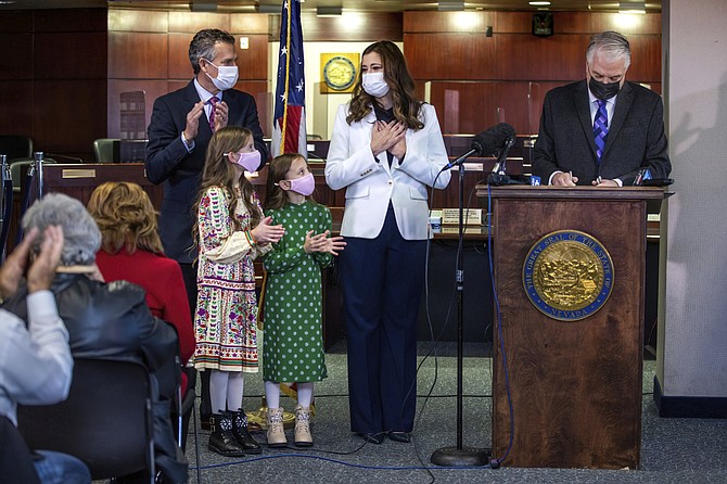 Nevada Gov. Steve Sisolak, right, signs the official document to appoint Lisa Cano Burkhead, second from right, as new lieutenant governor during a news conference at the Grant Sawyer Building on Dec. 16, 2021, in Las Vegas, as Burkhead's husband Jeffery, from left, daughters Raquel, 9, and Sofia, 8, look on. (L.E. Baskow/Las Vegas Review-Journal via AP)