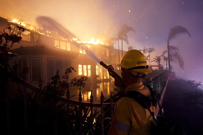 A firefighter works to put at a structure burning during a wildfire Wednesday in Laguna Niguel, Calif.