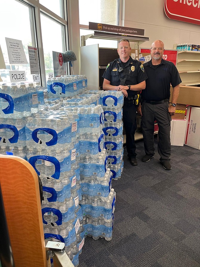 Fallon police officers Daniel Groom, left, and Sgt. John Riley stand next to June’s collection of water. Cases will be collected and then donated to local first-responders through August.