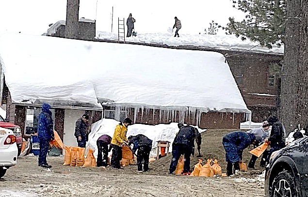 Dozens of people fill up sandbags Thursday while firefighters clear the roof at a South Lake Tahoe fire station.