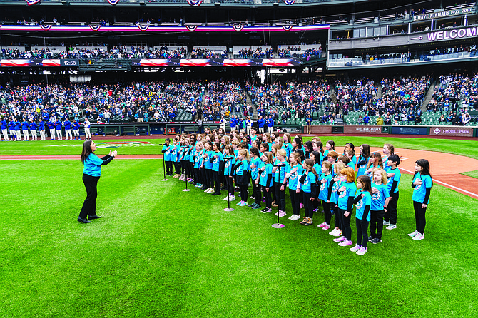 Coe Elementary School performing arts program director Krista Carreiro directs 77 elementary students as they sing the national anthem at the Mariners’ opening weekend game on Sunday. Carreiro has taught at Coe for 30 years, instilling a love for the arts in the students.