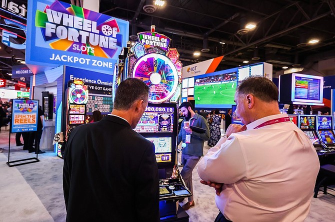 Global Gaming Expo attendees discuss a Wheel of Fortune slot machine at the IGT booth during the tradeshow on Oct. 11, 2022.