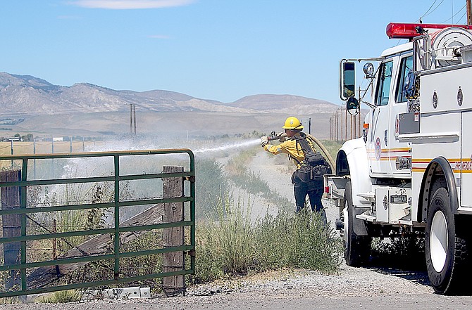 An East Fork firefighter douses a fire just off Muller Lane on Tuesday afternoon.