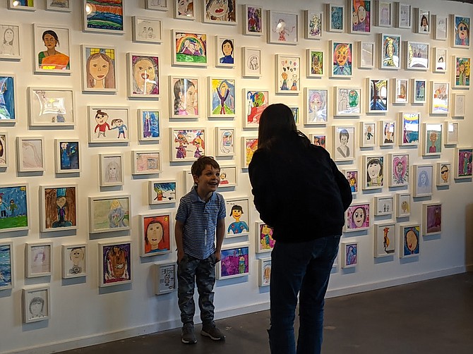 An elementary school artist poses with their portrait at the Mother's Day art celebration in the Emergence Room gallery.