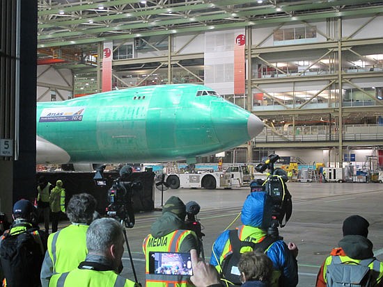 The final Boeing 747 begins to peek out from the factory floor as a tug pulls it.