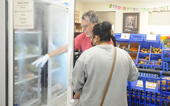 Snohomish Community Food Bank volunteer Mike Manley talks helps a client with what's in one of the food bank's freezers during the food bank’s Friday, May 12 service time to shop for supplemental food.