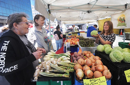 Jayden of A.C.M.A Mission Orchards out of Quincy, holds up a head of cabbage, as Janet Gore (far left) of Everett reacts with excitement at the Everett Farmers Market on Sunday, June 3. Gore had been in search of a head of cabbage to finally find the only vendor with them on that day.