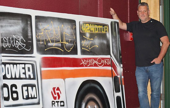 John Carswell stands in front of a piece of his graffiti collection. The collection will be shown at his museum that's being opened during this fall in Everett. The art piece depicts what Carswell called "mobbing" where a group of grafitti artists would run up to a bus at one of its stops and spray graffiti onto its side until it leaves the stop.