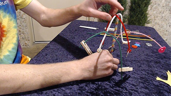 Nick Spicher works with the “Balancing Act” project in this screenshot from the project’s instruction video. “Balancing Act” involves balancing weights to create a kinetic sculpture.