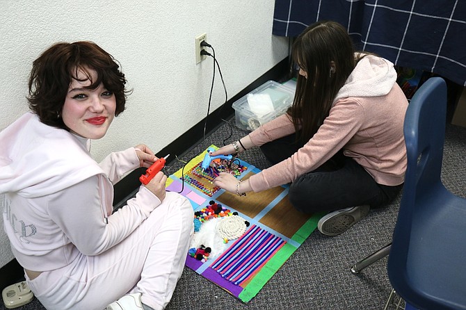 Carson High School sophomores Alexis Ross, left and Kylee Halverson create a sensory board using rhinestones and other products to help explain how one can be done with a posterboard or cardboard in their Early Childhood Education II class.