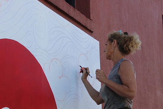 Gina Haugen touches up a cloud with pencil before painting it black. The mural is located on the east side of her shop, facing Avenue C and those heading west on First Street.