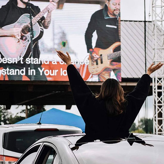 A woman raises her arms from the sunroof of a car during a recent Sunday service hosted by Gold Creek Community Church held at Thomas Family Farms, where the church uses a big screen to broadcast the sermon and activities.