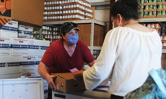 Sky Valley Food Bank volunteer Terri Picchi (left) hands a full case of frozen Cornish game hens to a client at the food bank in Monroe on Wednesday, July 15.