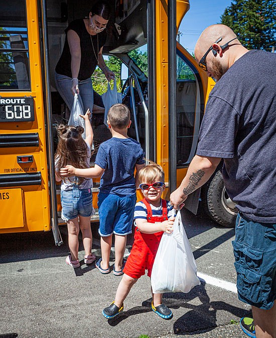 Two-year-old Louie Bauer and dad Jonathan get a lunch and breakfast sack, as his big brother Abel, and sister Mila wait their turn in the bus door near Emerson Elementary as part of the Snohomish School District’s continued meal services while classrooms are closed. Abel and Mila said they both miss their school classes and friends. Details and meal routes for Snohomish are online at www.sno.wednet.edu/covid19meals
