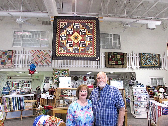 Quilt House owners Janet and Gary Pierce stand under the “House Warming” quilt that was featured in the 2004 edition of Better Homes Magazine’s Quilt Sampler. The shop is celebrating 25 years.