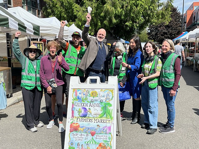 City Councilmembers Bob Kettle, center, and Tanya Woo (blue dress) joined staff and volunteers to ring the opening bell of the season’s first Queen Anne Farmer’s Market.