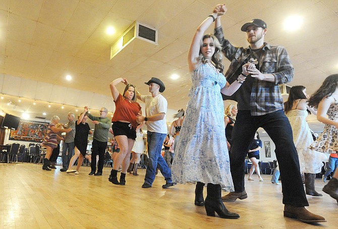 Darrin Obee (cowboy hat, in center) and his wife Ashley (red top), along with Brandon Bixel and Shantell Benton (white and blue dress, at right), all from Marysville, practice a couples dance moves as instructors Jen and Brian Workman demonstrate from the stage during a class in country dancing at Normanna Hall in Everett on Tuesday, June 25.