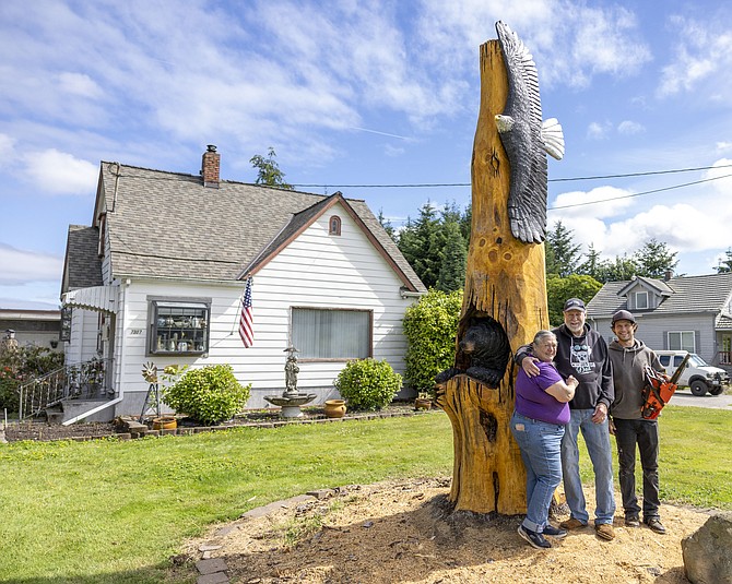 Donita Schacklin, Dennis Schacklin and Marcus Janssen pose with the carving Janssen made of a soaring eagle and a bear in the tree in front of the Schacklins’ house in Snohomish on June 28. The carving took nine days to make and is made of a ponderosa pine the Schacklins planted more than 40 years ago.