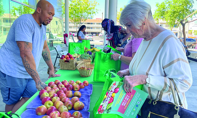 Jannelle Calderon • The Nevada Independent
DruMaine Davis, co-owner of Prevail Marketplace, talking to a customer choosing apples during a pop-up produce stand event aimed to address food insecurity at the Bonneville Transit Center in Downtown Las Vegas on Sept. 5, 2023.