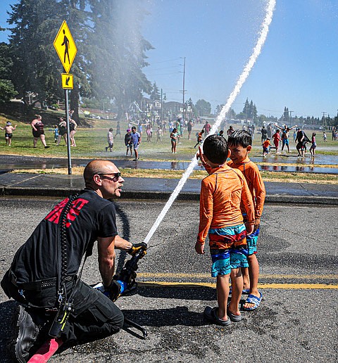 Everett firefighter John Poyner demonstrates hose work with Marshall and Walter, age 8 and 6, who came from Mukilteo with their mom for a water cool off day put on by the Everett Fire Department Saturday, July 20 at  Wiggums Hollow Park in north Everett.
A second hose day will be Saturday, Aug. 24 at Walter E. Hall Park, 1226 W. Casino Road, from 3-3:30 p.m.
Firefighters sprayed the crowd from two nozzles attached from Everett Fire’s Truck E-2, including the truck’s top-mounted big hose. The unit is captained by Joel Sellenger.