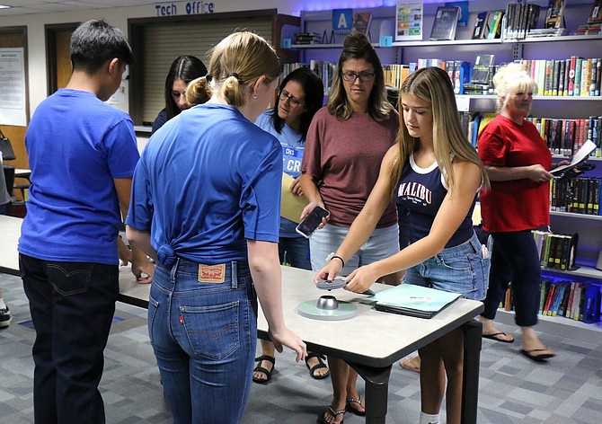 Freshmen and Blue Crew members Jaiden Joaquin, far left, and Hannah Ingram, show how to unlock a Yondr cell phone pouch.