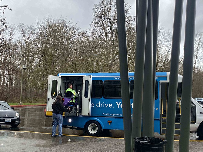 Mike Gantala, wearing green, rises into a transportation van to give him a ride to where-ever the man with cerebral palsy needed to go. The Homage program gives qualifying rural and semi-rural  residents who live too far away to get Dial-A-Ride-Transportation (DART).