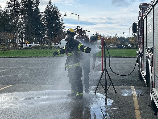 A Snohomish firefighter in gear is sprayed with one of the department’s new StormStick decontaminating devices that is attached to a fire engine on Tuesday, Nov. 12.  One firefighter wears full gear while the StormStick sprays them with soapy water, while another firefighter scrubs their gear with a bristle brush.