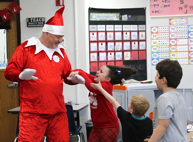 Mark Twain Elementary School Vice Principal Mark Rodina, dressed as the Elf on the Shelf, visits first-grade teacher Jill Schwartz’s classroom Dec. 19 and greets Leila Hermo, center.