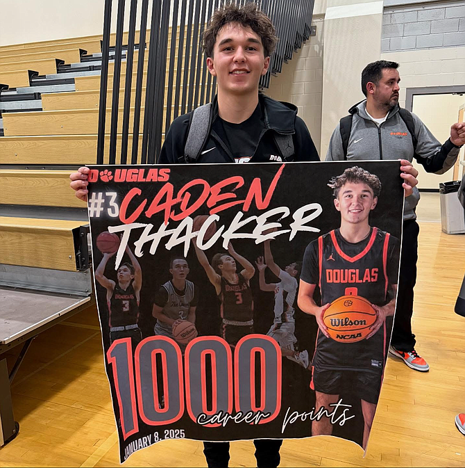 Douglas High senior Caden Thacker poses with a banner after scoring 1,000 points in his career, following eight points against Spanish Springs on Wednesday.