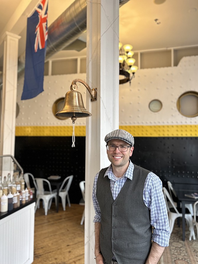 Top It Yogurt Shoppe owner Ken Coman stands in front of his home-built, exact-size Titanic wall piece in his shop on Saturday, March 8.