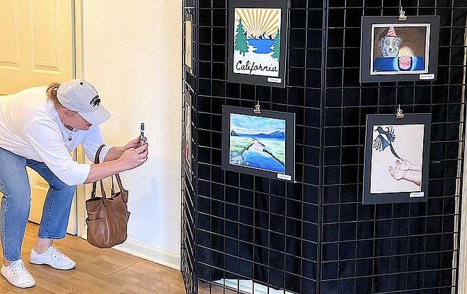 A visitor crouches to get a photo of one of the pieces at the reception for Douglas High School artists at the Copeland Gallery on Saturday.