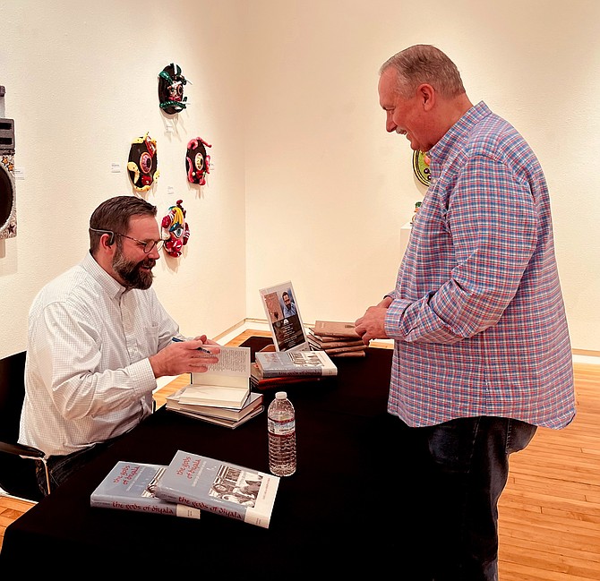 Caleb Cage, left, signs a copy of his book, ‘Desert Mementos: Stories of Iraq and Nevada (Battle Born),’ for Mayor Ken Tedford at the Churchill Arts Council presentation April 12.