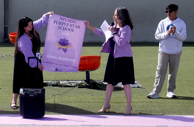 Oasis Academy K-8 principal Amanda Barbosa, left, holds the Purple Star school banner with KellyLynn Charles, Purple Star coordinator from the Nevada Department of Education, at a presentation on Thursday. Looking on is student Neel Bhakta.
