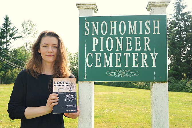 Taylor Russell holds her book for a portrait at the Snohomish Pioneer Cemetery sign.