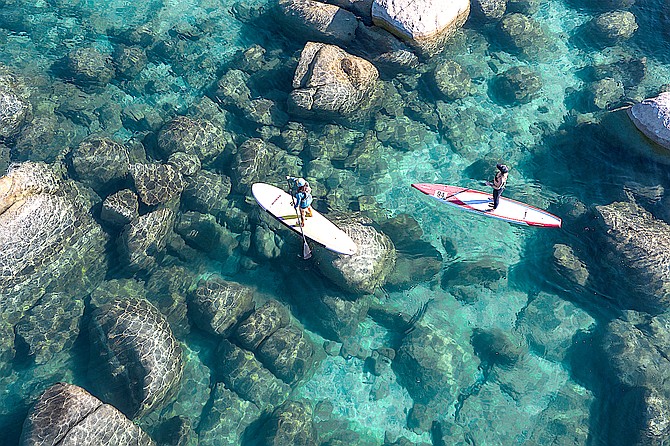 Paddleboarders floating on Lake Tahoe. Hand-launched vessels can carry aquatic invasive species and must be Clean, Drain, and Dry before moving to other lakes or other parts of Lake Tahoe.