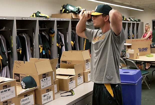 Oakland Athletics catcher John Jaso tries on a hat in the locker room for spring training baseball practice Friday, Feb. 14, 2014, in Phoenix. Athletics pitchers and catchers reported to camp Friday for physicals before beginning training Saturday. (AP Photo/Gregory Bull)