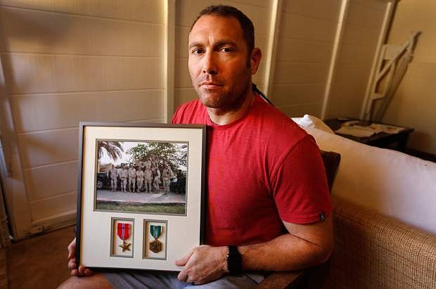 FILE - In this Friday, Oct. 21, 2016 file photo, Robert D&#039;Andrea, a retired Army major and Iraq war veteran, holds a frame with a photo of his team on his first deployment to Iraq in his home in Los Angeles. Nearly 10,000 California National Guard soldiers have been ordered to repay huge enlistment bonuses a decade after signing up to serve in Iraq and Afghanistan, the Los Angeles Times reported Saturday. (Al Seib/Los Angeles Times via AP, File)