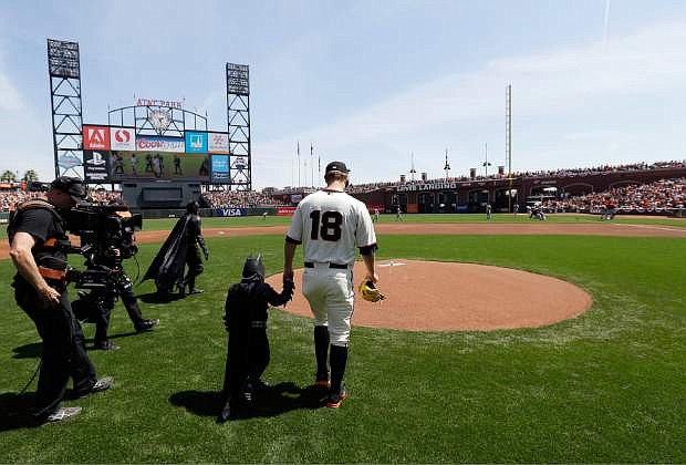 Miles Scott, dressed as Batkid, second from right, walks to the mound with San Francisco Giants pitcher Matt Cain (18) to throw the ceremonial first pitch before a home opener baseball game between the Giants and the Arizona Diamondbacks in San Francisco, Tuesday, April 8, 2014. On Nov. 15, 2013, Scott, a Northern California boy with leukemia, fought villains and rescued a damsel in distress as a caped crusader through The Greater Bay Area Make-A-Wish Foundation. (AP Photo/Eric Risberg, Pool)