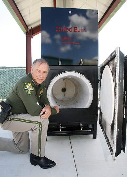 Carson City Sheriff Ken Furlong kneels next to a dual-chamber burner that will be used to incinerate contraband.