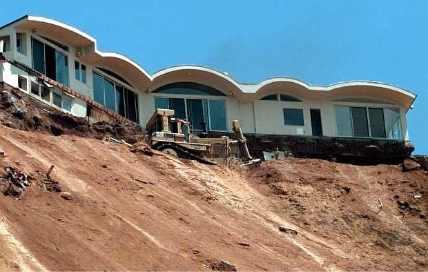 FILE - In this June 25, 1998 file photo, a Caltrans bulldozer terraces a sliding hillside below the condemned home above Pacific Coast Highway near Las Flores Canyon Road in Malibu, Calif. The home and at least one other at the top of the slide was scheduled for demolition. Federal meteorologists said Thursday that the current El Nino is already the second strongest on record for this time of year and could go down as one of the most potent weather changers of the past 65 years. The National Oceanic Atmospheric Administration recorded unusual warmth in the Pacific Ocean the last three months. El Nino is a heating of the equatorial Pacific that changes weather worldwide, mostly affecting the United States in winter.  (AP Photo/Reed Saxon, File)