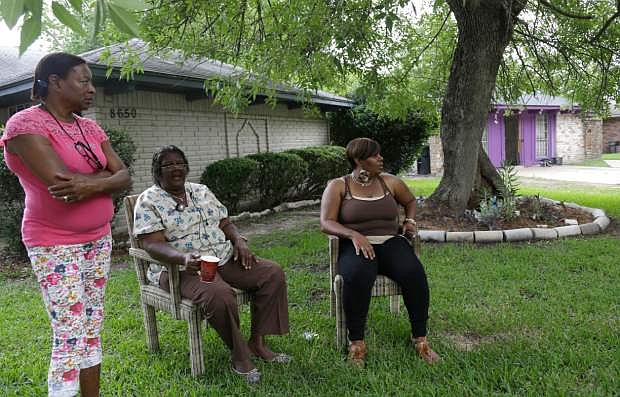Neighbors watch from their yard as authorities investigate a home, right background, Friday July 19, 2013, in Houston where police say four homeless men were found in deplorable conditions. Officers who responded to a call expressing concern said said they found three men locked in a garage and a fourth in the home who were malnourished and may have been being held so a captor could cash checks the men were receiving. One person was taken into custody. (AP Photo/Pat Sullivan)