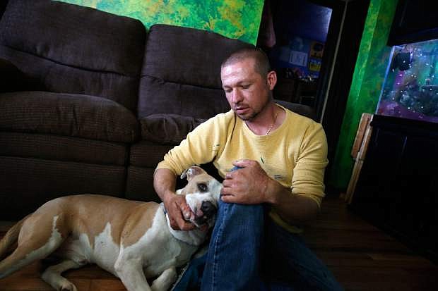 In this May 1, 2014 photo, Wayne Winkler, who suffered burns to 12 percent of his body when butane fumes ignited while he was making hash oil at home, pets his dog Bailey, in his living room, in Denver. Since marijuana became legal on Jan. 1, the state has seen nearly three dozen explosions caused by people making pot concentrates at home, and authorities are grappling with what to do about it. (AP Photo/Brennan Linsley)