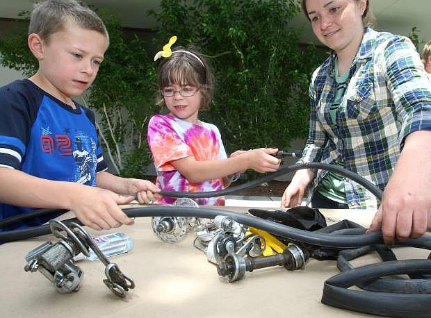 Twins Thomas and Linda Bathgate, 8, learn about repairing a flat bicycle tire from Spokes America cyclist Maddie Hickman at the library on Monday.